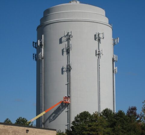 Field Painting of cellular communications equipment to match tank color utilizing a boom lift. Communications Equipment