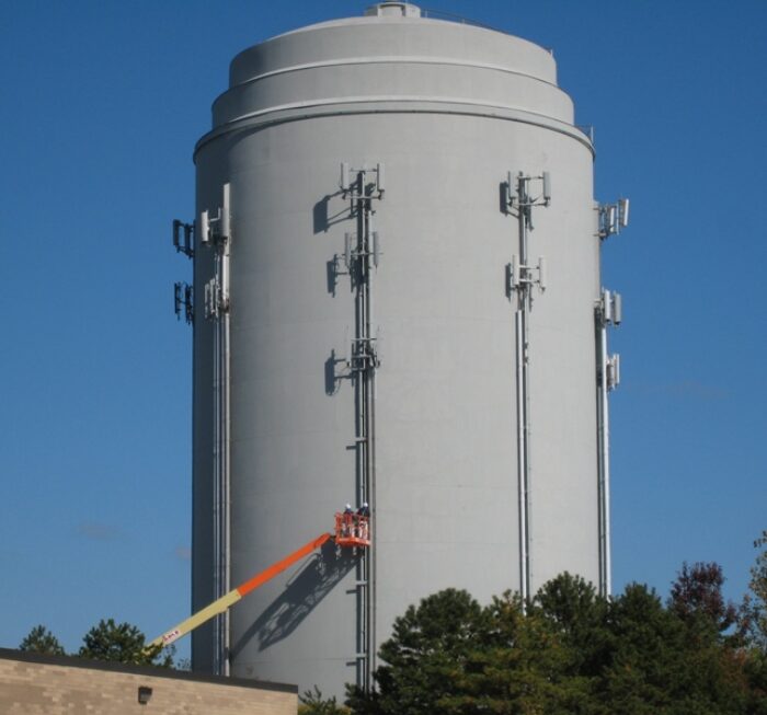 Field Painting of cellular communications equipment to match tank color utilizing a boom lift. Industrial Communications Equipment Painting